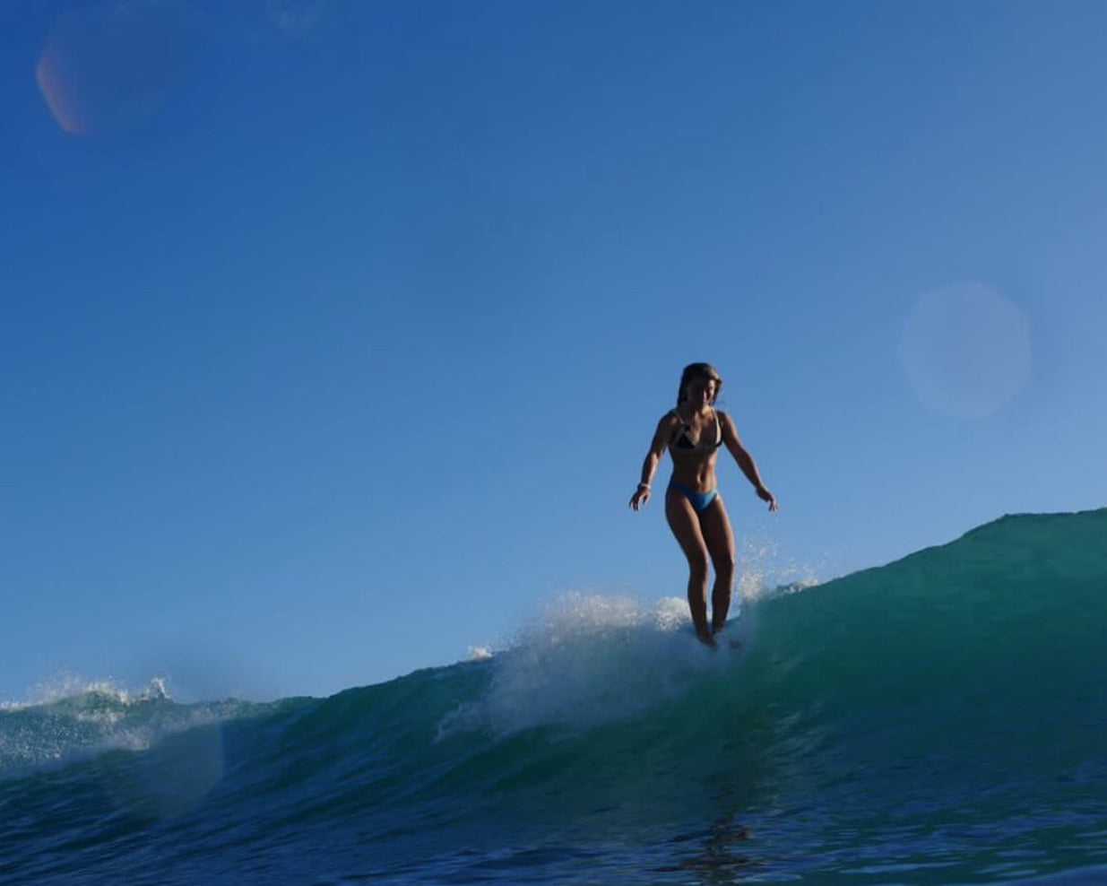 Person surfing on a wave with clear blue sky