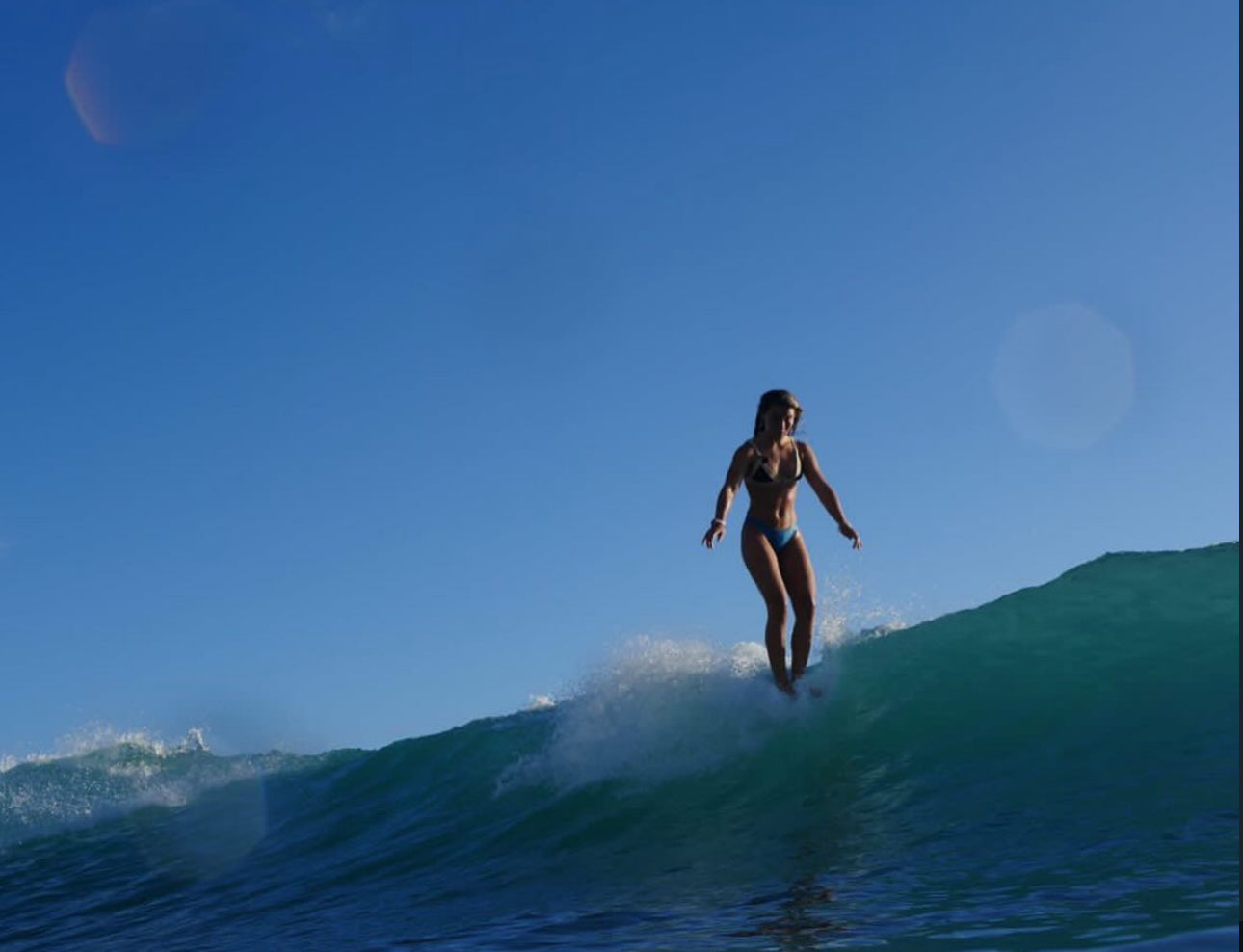Person surfing on a wave with clear blue sky